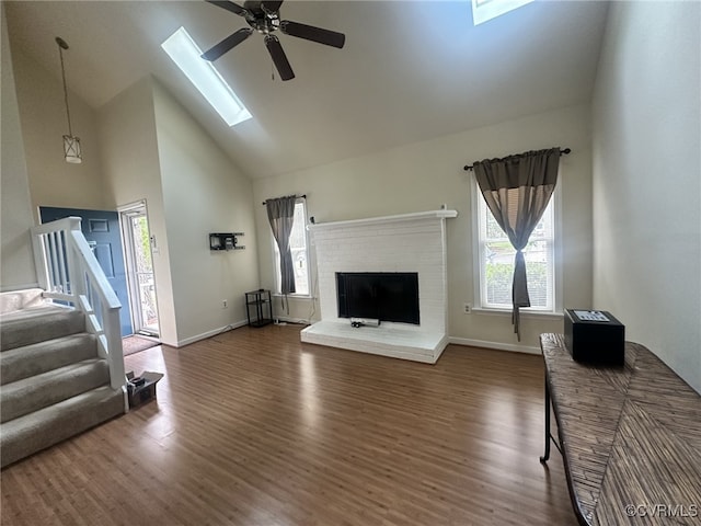 living room with plenty of natural light, high vaulted ceiling, a skylight, and wood finished floors