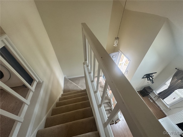 staircase with a towering ceiling, carpet flooring, and baseboards