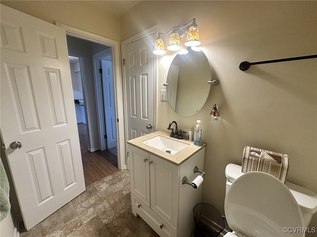 bathroom with toilet, stone finish flooring, and vanity