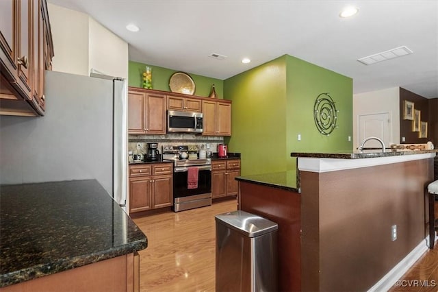 kitchen with visible vents, brown cabinetry, light wood-style floors, and stainless steel appliances