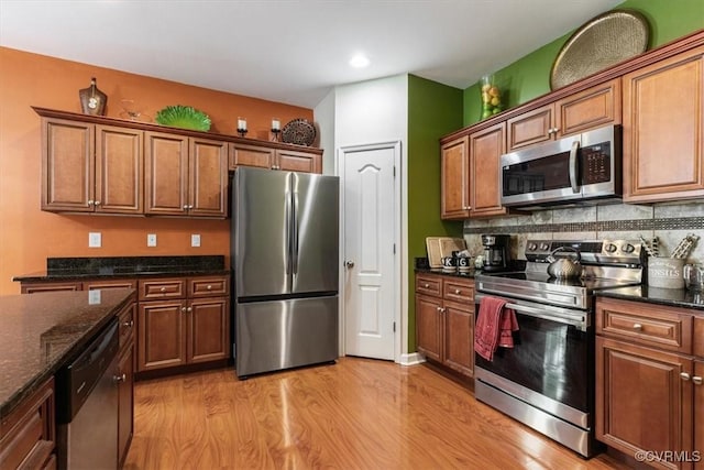 kitchen featuring tasteful backsplash, stainless steel appliances, light wood finished floors, and dark stone countertops