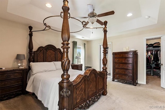 bedroom with a closet, light carpet, a walk in closet, recessed lighting, and a tray ceiling