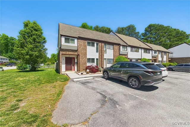 multi unit property featuring brick siding, uncovered parking, and a front lawn