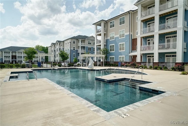 community pool with a patio, a jacuzzi, fence, and a residential view