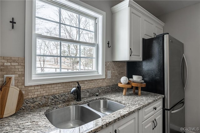 kitchen with white cabinets, a sink, freestanding refrigerator, a healthy amount of sunlight, and backsplash