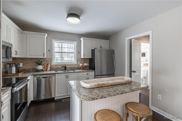 kitchen with a sink, a kitchen breakfast bar, dark wood finished floors, stainless steel appliances, and tasteful backsplash