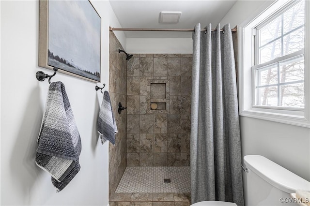 bathroom featuring toilet, tiled shower, and visible vents
