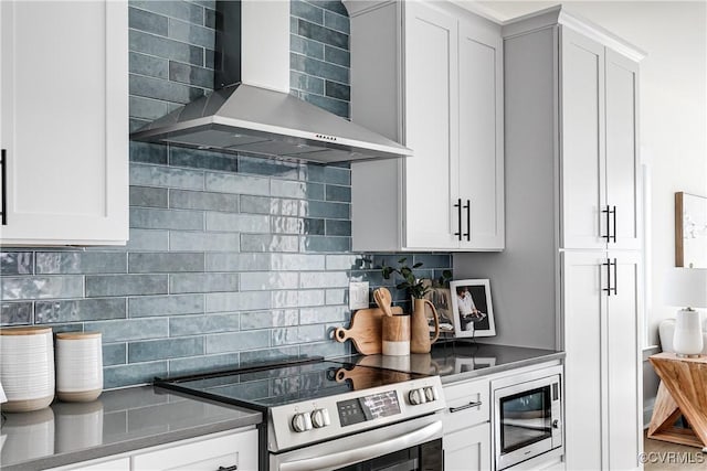 kitchen with white cabinets, dark countertops, appliances with stainless steel finishes, wall chimney exhaust hood, and tasteful backsplash