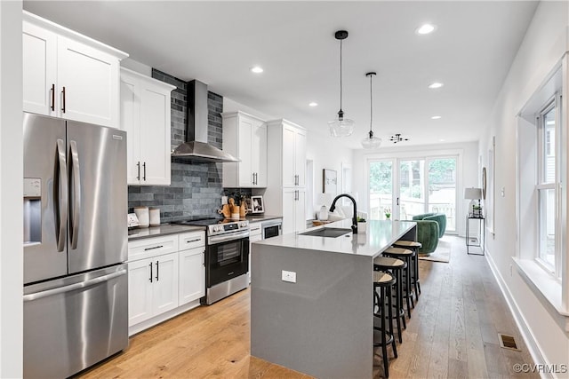 kitchen featuring a breakfast bar area, appliances with stainless steel finishes, a sink, wall chimney exhaust hood, and an island with sink