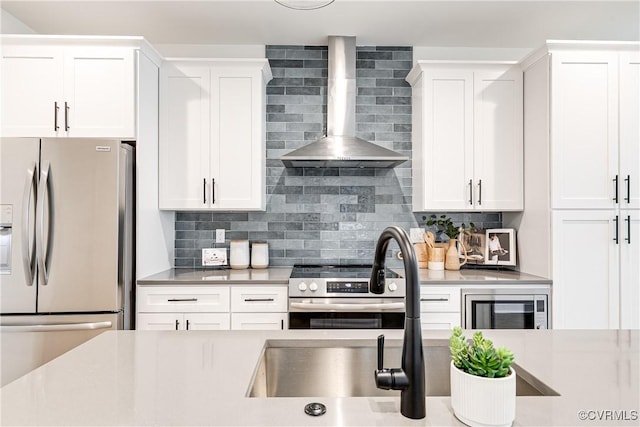 kitchen with wall chimney range hood, decorative backsplash, stainless steel appliances, and white cabinetry