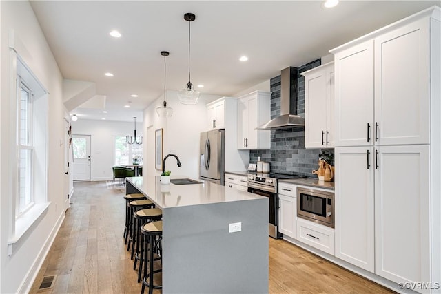 kitchen featuring a kitchen island with sink, wall chimney range hood, a kitchen bar, a sink, and stainless steel appliances