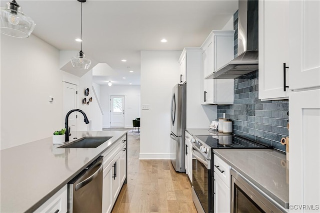 kitchen featuring wall chimney range hood, white cabinets, appliances with stainless steel finishes, a sink, and light wood-style flooring
