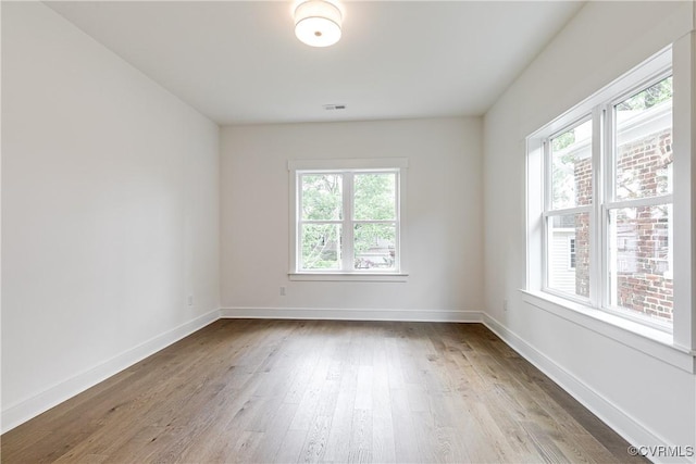 unfurnished room with visible vents, baseboards, wood finished floors, and a healthy amount of sunlight