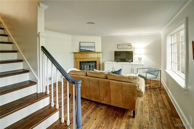 living area with a glass covered fireplace, dark wood finished floors, stairs, baseboards, and ornamental molding
