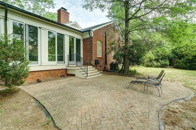 rear view of house with brick siding, a patio area, and a chimney