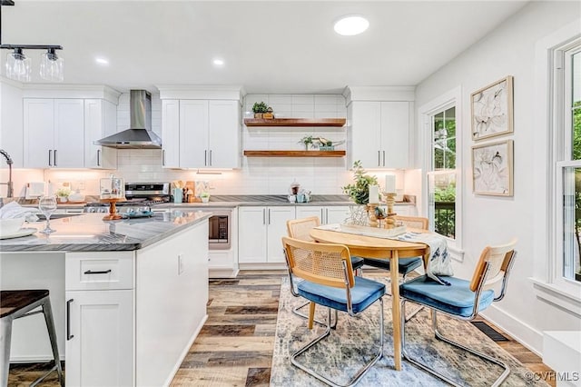 kitchen with tasteful backsplash, wall chimney exhaust hood, white cabinets, stainless steel range oven, and light wood-style flooring