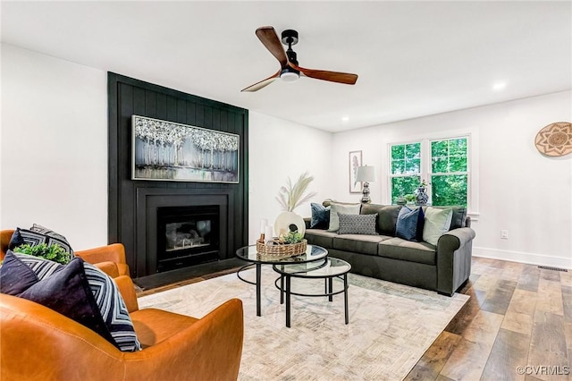 living room with ceiling fan, a fireplace, baseboards, visible vents, and hardwood / wood-style flooring