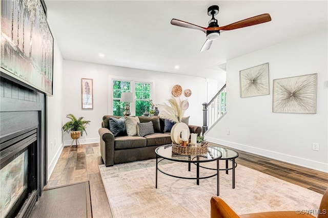 living area with stairs, baseboards, a large fireplace, and wood finished floors