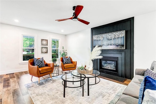 living area with ceiling fan, a large fireplace, recessed lighting, baseboards, and wood finished floors