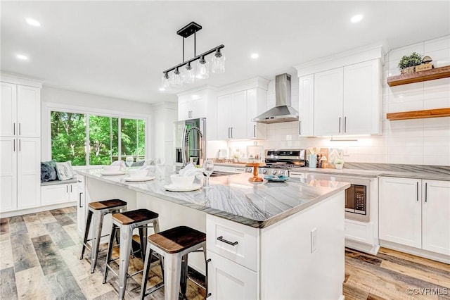 kitchen featuring wall chimney range hood, appliances with stainless steel finishes, white cabinets, and light wood-type flooring