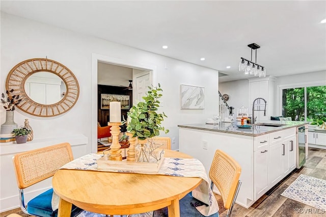 kitchen featuring hanging light fixtures, stainless steel dishwasher, white cabinetry, a sink, and light wood-style flooring