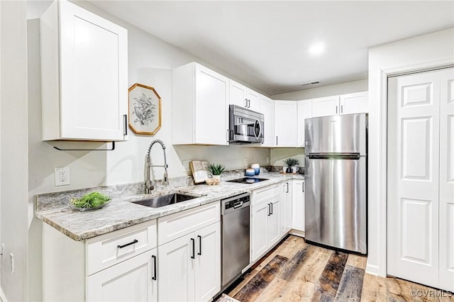 kitchen with stainless steel appliances, white cabinetry, a sink, and light wood finished floors