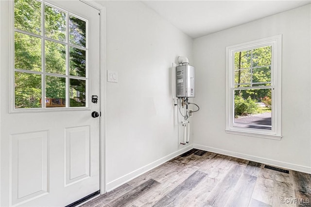 doorway featuring baseboards, water heater, wood finished floors, and visible vents