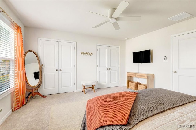 carpeted bedroom featuring two closets, baseboards, visible vents, and ceiling fan