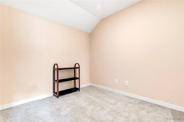 spare room with baseboards, vaulted ceiling, and light carpet