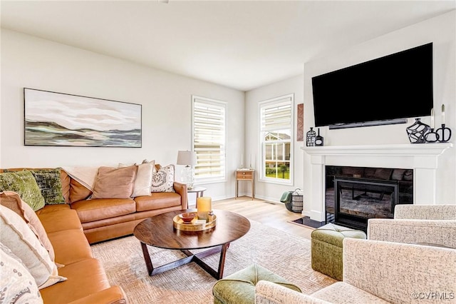 living room featuring a fireplace with flush hearth, baseboards, and wood finished floors