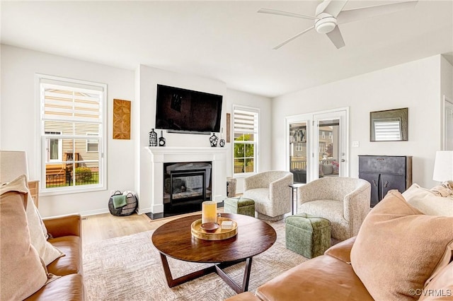 living room featuring baseboards, ceiling fan, a glass covered fireplace, and wood finished floors