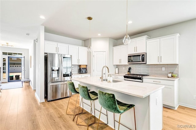 kitchen featuring decorative backsplash, light wood-style floors, a kitchen breakfast bar, a sink, and stainless steel appliances