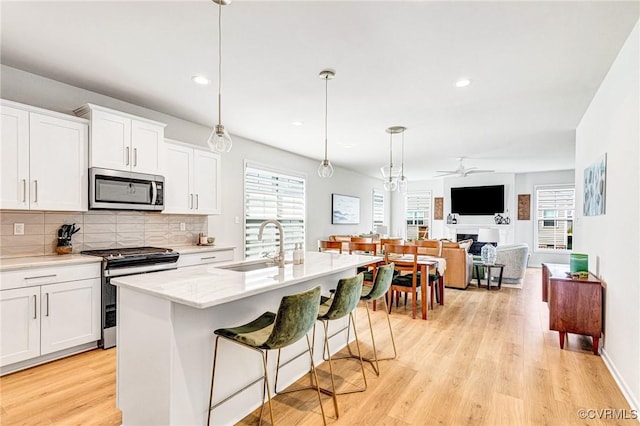 kitchen featuring decorative backsplash, a ceiling fan, appliances with stainless steel finishes, a sink, and light wood finished floors