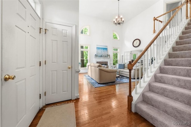 foyer with a fireplace, wood finished floors, stairway, a notable chandelier, and a high ceiling