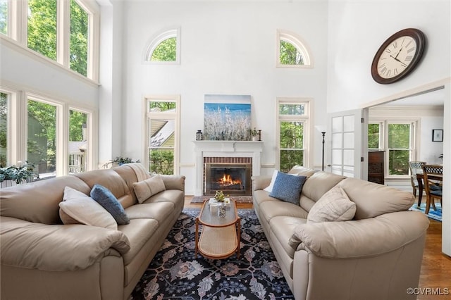 living room with a brick fireplace, a high ceiling, plenty of natural light, and wood finished floors