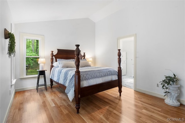 bedroom with baseboards, vaulted ceiling, and light wood finished floors