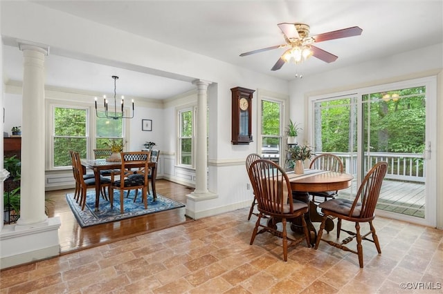 dining area featuring ornate columns, stone finish flooring, ceiling fan with notable chandelier, and a wainscoted wall