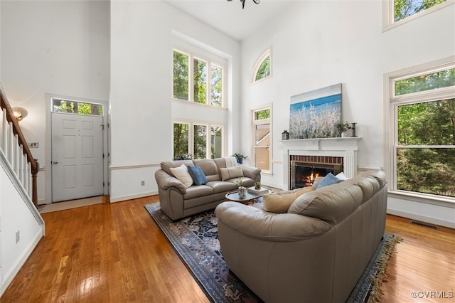 living room with visible vents, a fireplace, hardwood / wood-style flooring, baseboards, and a high ceiling