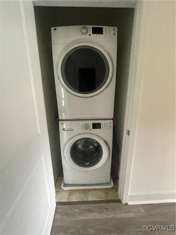 laundry area featuring baseboards, laundry area, wood finished floors, and stacked washer and clothes dryer