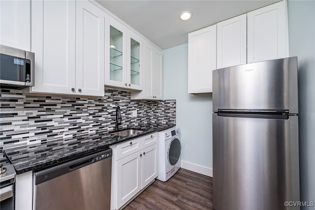 kitchen featuring a sink, washer / clothes dryer, stainless steel appliances, dark stone counters, and glass insert cabinets