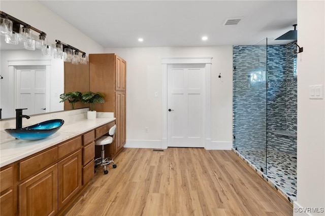 full bathroom featuring visible vents, a tile shower, wood finished floors, vanity, and recessed lighting
