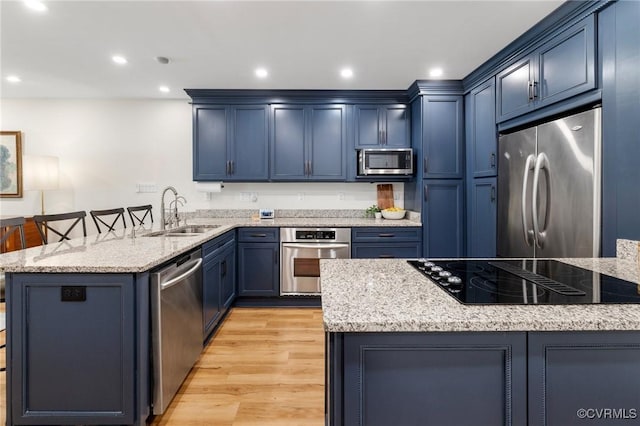 kitchen with light stone counters, a sink, blue cabinetry, stainless steel appliances, and a peninsula