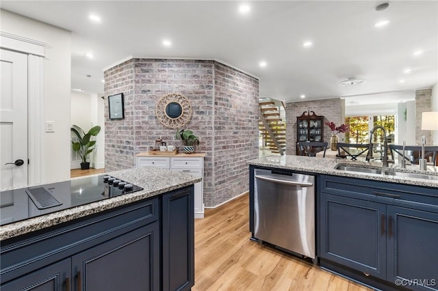 kitchen featuring brick wall, stainless steel dishwasher, light stone countertops, a sink, and light wood-style floors
