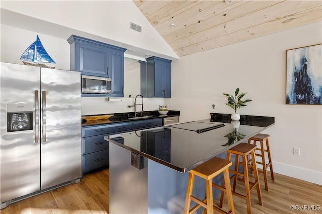 kitchen featuring a kitchen breakfast bar, appliances with stainless steel finishes, dark countertops, a sink, and lofted ceiling