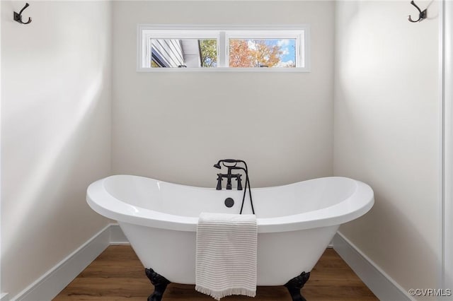 bathroom featuring a freestanding bath, baseboards, and wood finished floors