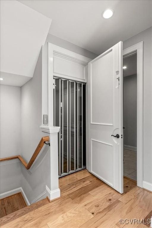 corridor with baseboards, recessed lighting, light wood finished floors, and an upstairs landing
