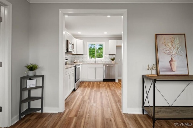 kitchen with crown molding, appliances with stainless steel finishes, backsplash, and light wood finished floors