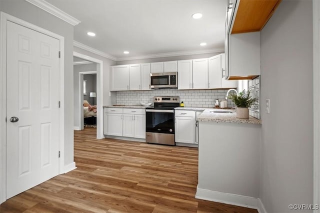 kitchen featuring appliances with stainless steel finishes, light wood-type flooring, a sink, baseboards, and ornamental molding