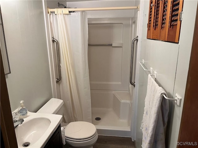 bathroom featuring wood finished floors, a stall shower, toilet, and vanity
