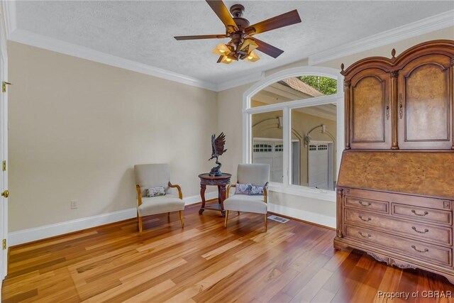 living area with a ceiling fan, a textured ceiling, visible vents, baseboards, and light wood finished floors